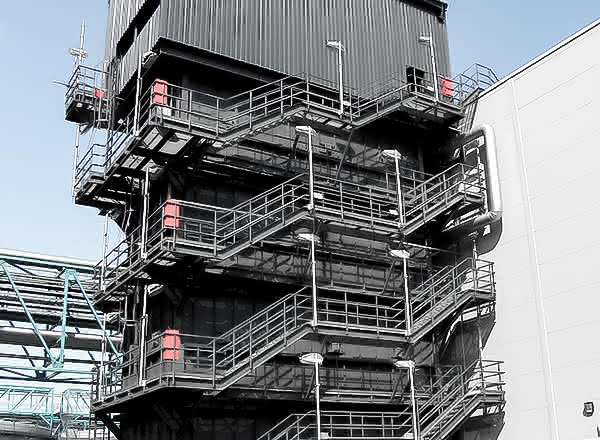 Multi-level industrial MAHLER Hydroform C tower with external steel staircases and platforms beside a larger plant building under a clear blue sky.