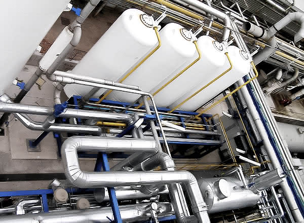 Close-up view of a MAHLER HYDROSWING system showing several large white horizontal pressure vessels mounted above a dense network of stainless-steel pipes, valves, and blue support frames inside an industrial plant.