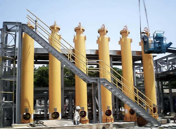 MAHLER HYDROSWING adsorption unit with multiple tall yellow vessels in a row, connected by steel platforms and a diagonal staircase, shown at an industrial site with workers nearby.