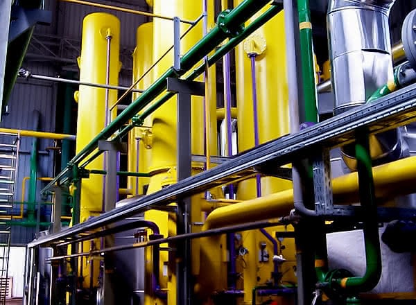 Industrial protective gas system with multiple tall yellow pressure vessels, green and black pipework, and metallic ducts inside a production hall.