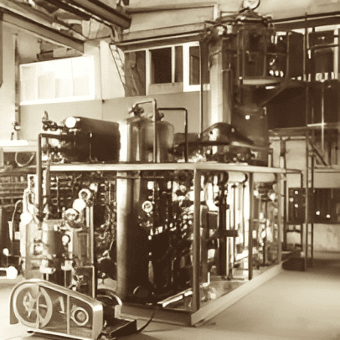 Vintage sepia photo of an early MAHLER gas generation plant inside a workshop, showing large cylindrical vessels, piping, and control equipment on a skid.