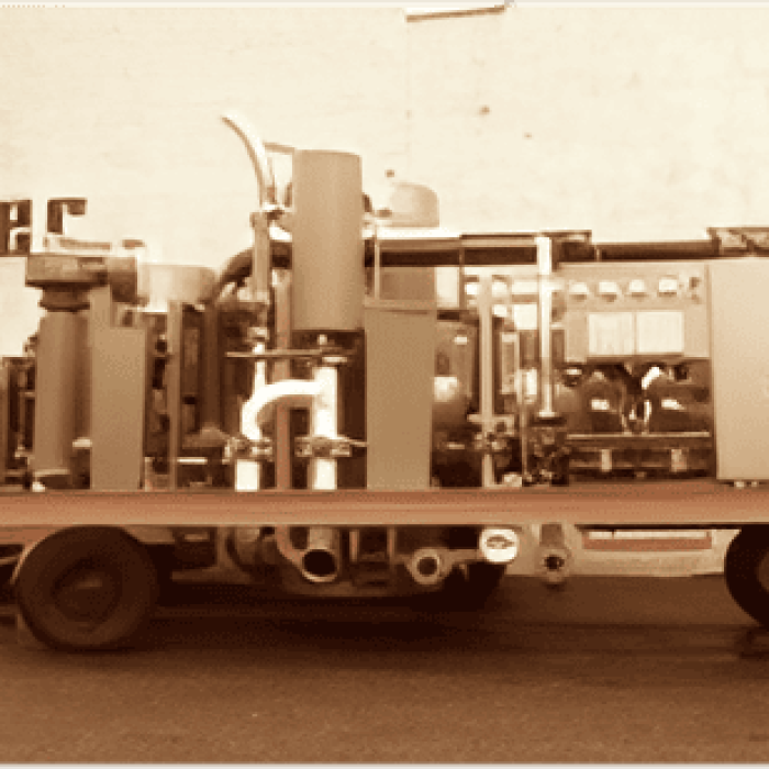 Vintage sepia photo of an early MAHLER gas plant mounted on a trailer, parked in front of a factory building with the “mahler” name on the wall.