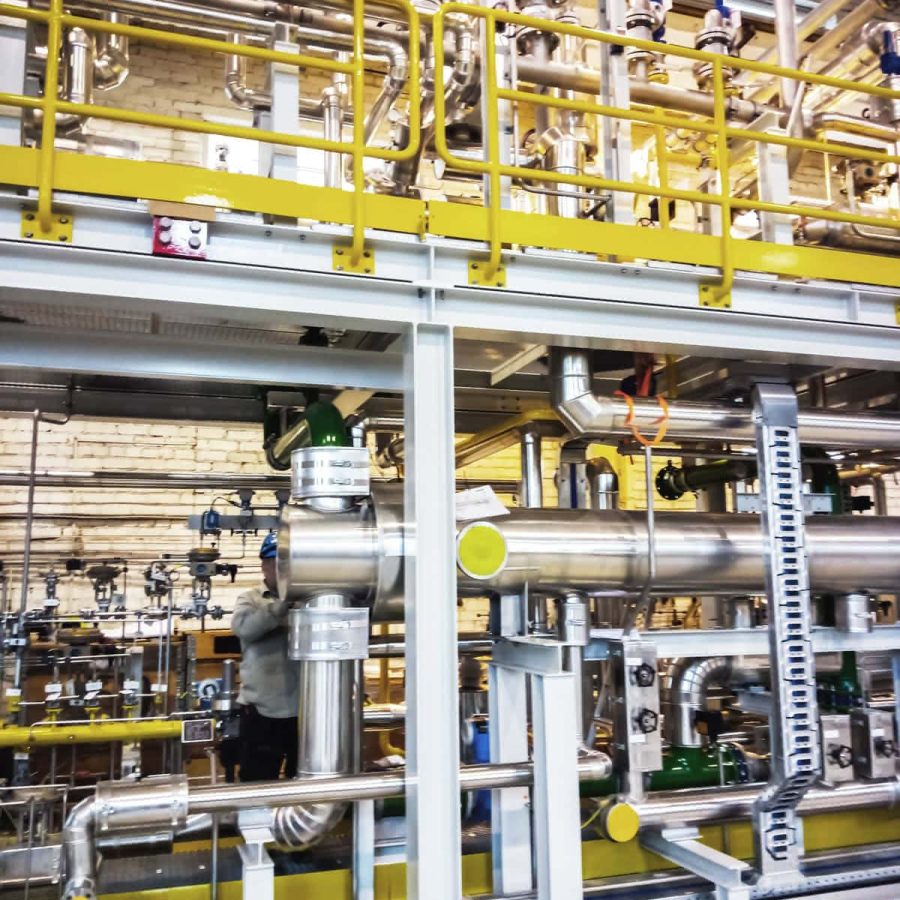 MAHLER gas plant module during assembly, featuring stainless steel piping and valves with a yellow safety-railed service platform in the workshop.