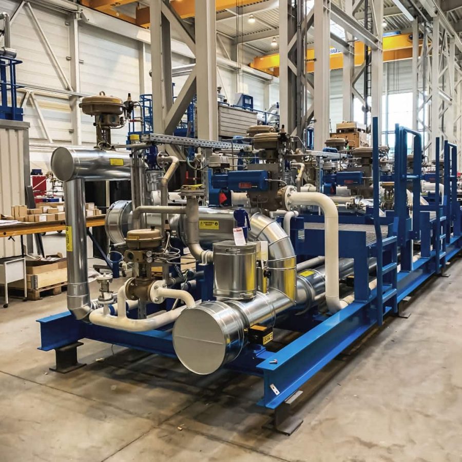 MAHLER gas plant skid in the manufacturing hall, with blue steel frame and stainless piping, valves, and control units ready for delivery.