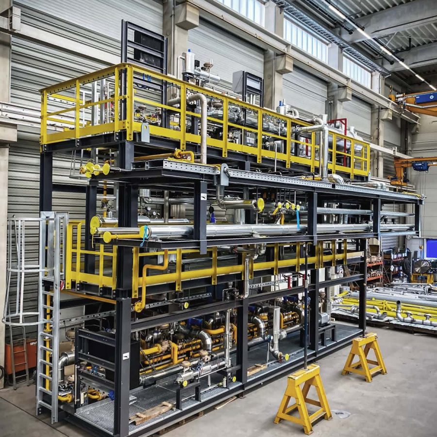 Large modular gas plant skid with yellow safety railings being assembled in a factory hall.