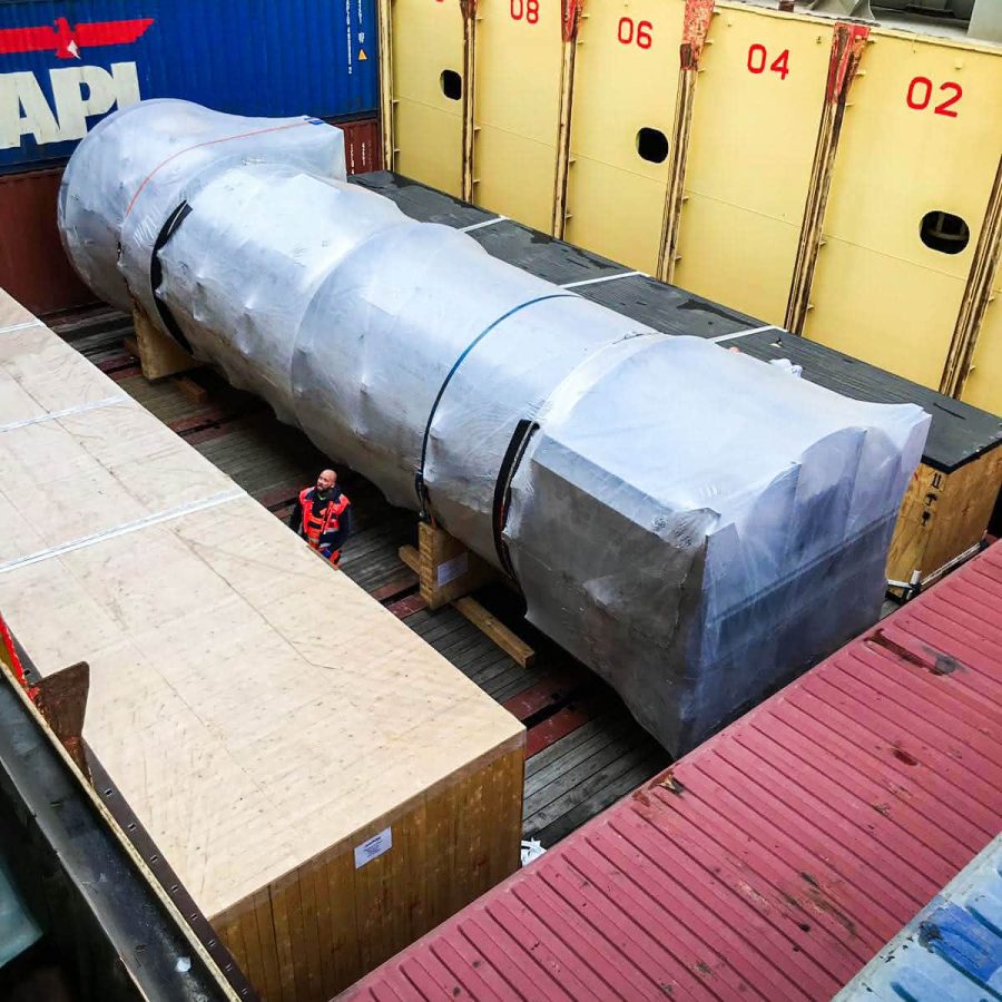MAHLER plant component wrapped for overseas shipment, secured in a cargo ship hold beside containers.