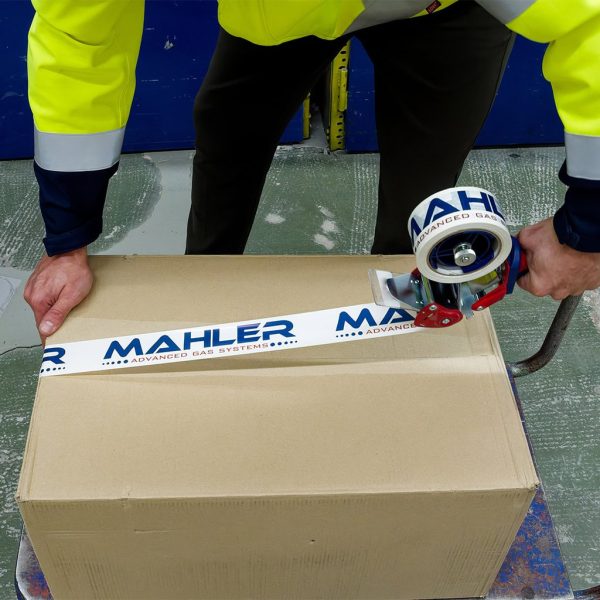 Worker in high-visibility jacket seals a cardboard box with Mahler Advanced Gas Systems branded tape using a handheld packing tape dispenser.