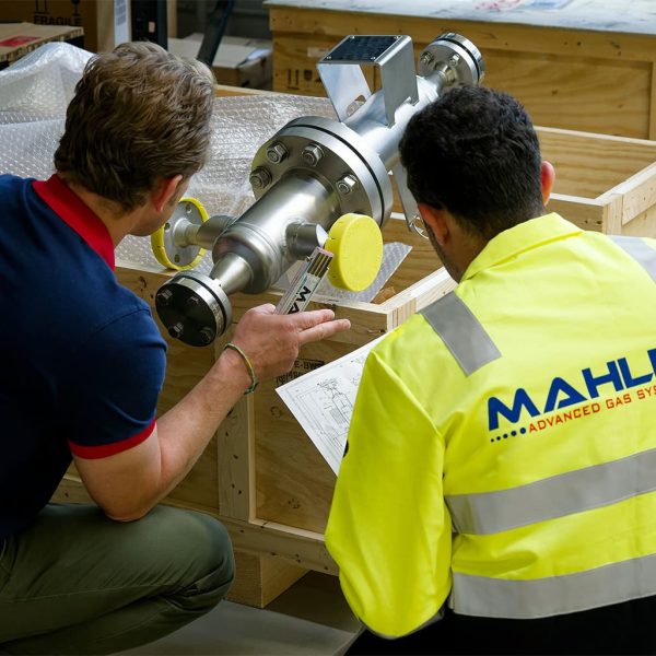 Two MAHLER AGS technicians review technical drawings while inspecting a large stainless-steel component in a wooden shipping crate.