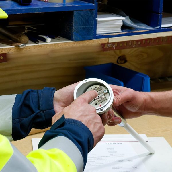 Technicians in safety jackets receive hands-on training, inspecting and wiring an electrical connector on a workbench.