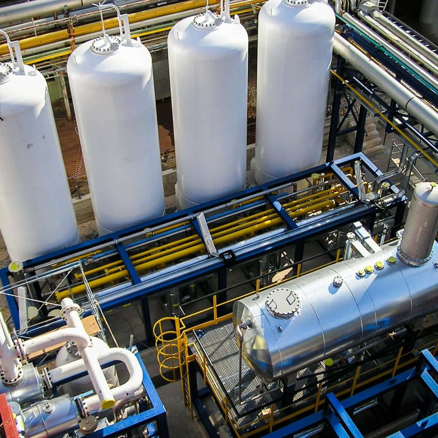 Top-down view of a MAHLER gas plant: four tall white storage vessels beside a steel skid with piping, a horizontal pressure tank, and yellow safety railings.